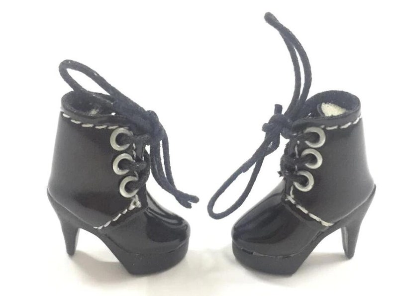 May include: A pair of black heeled boots with white stitching and silver eyelets. The boots have laces that tie at the top.