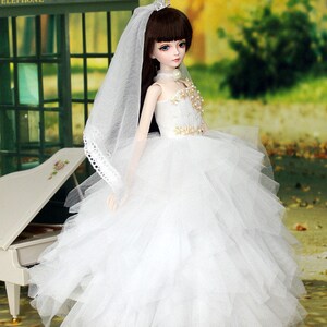 May include: A white bridal gown with a tulle skirt and a lace trim on the veil. The doll is wearing a tiara and a pearl necklace.