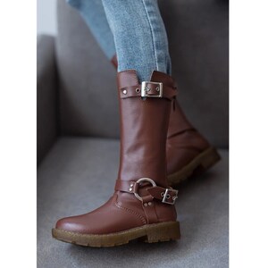 May include: Brown leather knee-high boots with silver buckles and a chunky heel.