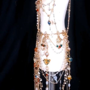 May include: A gold chain body jewelry piece with multiple strands of beads and charms. The piece features a variety of colors, including red, orange, green, and blue.