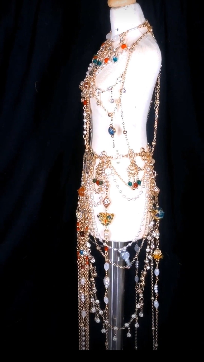 May include: A gold chain body jewelry piece with multiple strands of beads and charms. The piece features a variety of colors, including red, orange, green, and blue.