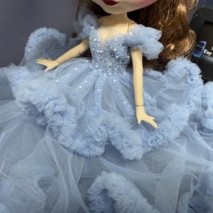 May include: A light blue tulle dress with a beaded bodice and ruffled trim. The dress is designed for a doll.