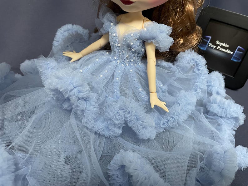 May include: A light blue tulle dress with a beaded bodice and ruffled trim. The dress is designed for a doll.