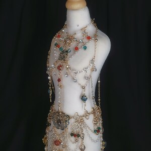 May include: A gold-toned jewelry set with a variety of beads and charms, including flowers, butterflies, and geometric shapes. The set includes a necklace, a belt, and a bracelet. The jewelry is displayed on a white mannequin.