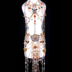 May include: A gold-toned body chain with multiple layers of chains, beads, and charms. The chain features a variety of colors, including red, orange, green, and blue. The chain is adorned with pearls, flowers, and other decorative elements.