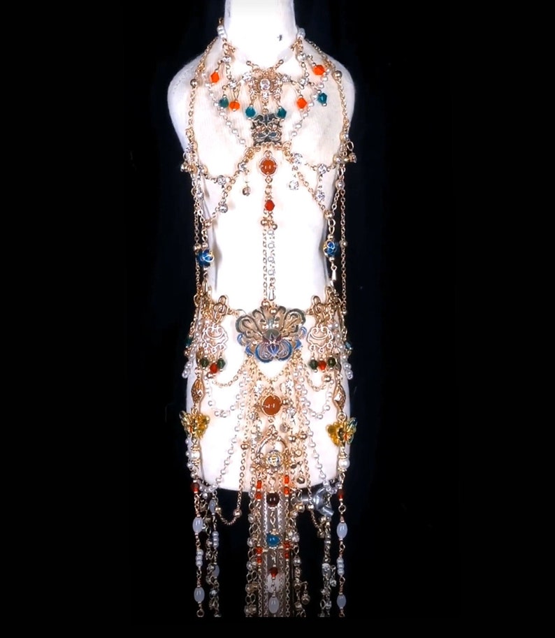 May include: A gold-toned body chain with multiple layers of chains, beads, and charms. The chain features a variety of colors, including red, orange, green, and blue. The chain is adorned with pearls, flowers, and other decorative elements.