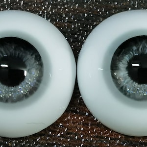 May include: A pair of gray doll eyes with silver glitter. The eyes are set in a white plastic base.