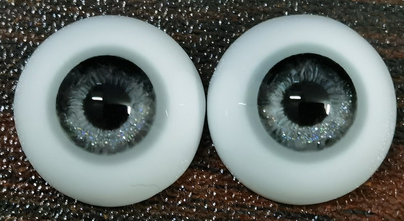 May include: A pair of gray doll eyes with silver glitter. The eyes are set in a white plastic base.