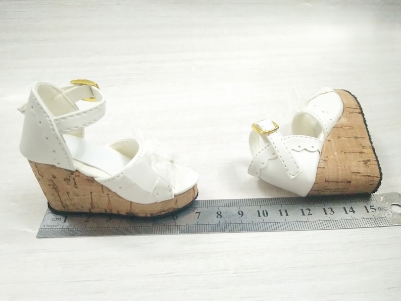 Peut inclure: Une paire de sandales compens&eacute;es blanches avec des talons en li&egrave;ge et des boucles dor&eacute;es. Les sandales mesurent 7 cm de long.