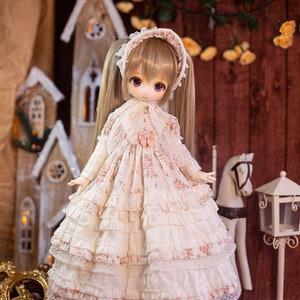 May include: A doll with long blonde pigtails wearing a white dress with pink floral accents and lace trim. The doll is standing on a rug with a wooden house and a white horse in the background.