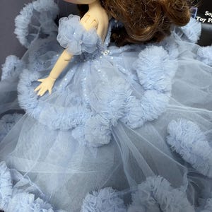 May include: A light blue tulle dress with ruffled trim and a beaded bodice. The dress is designed for a doll and has a long train.