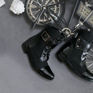 May include: A pair of black lace-up boots with buckles and pointed toes. The boots are made of a soft, textured fabric and have a sturdy sole.