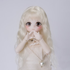 May include: A ball-jointed doll with long wavy platinum blonde hair, large brown eyes, and rosy cheeks. The doll wears a cream-colored sleeveless top with a delicate lace collar and a thin gold-toned chain necklace featuring a small heart pendant.