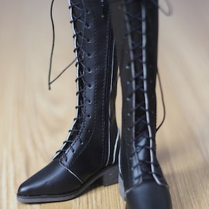May include: A pair of black leather boots with white stitching and laces. The boots have a pointed toe and a zipper on the inside of each boot.