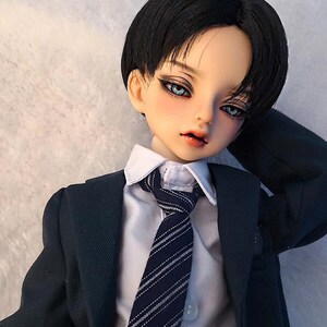 May include: A doll with black hair and blue eyes wearing a white shirt, a dark blue tie with white stripes, and a dark blue suit jacket.