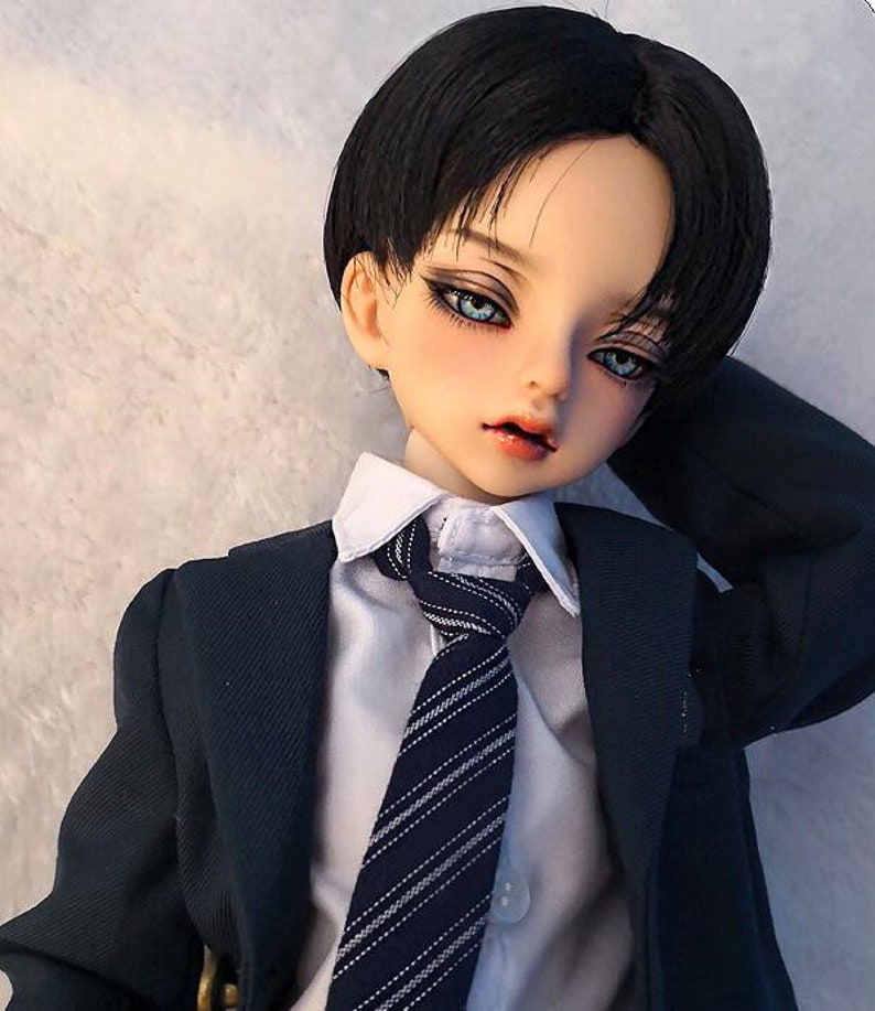 May include: A doll with black hair and blue eyes wearing a white shirt, a dark blue tie with white stripes, and a dark blue suit jacket.