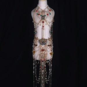 May include: A gold-tone body chain with red, green, and blue gemstones. The chain is made of multiple strands and features a butterfly pendant.
