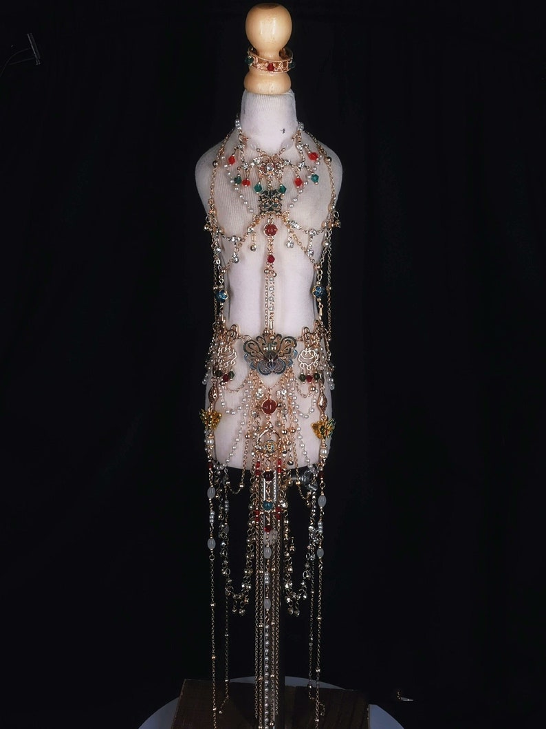 May include: A gold-tone body chain with red, green, and blue gemstones. The chain is made of multiple strands and features a butterfly pendant.