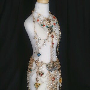 May include: A gold-toned body chain with multiple layers of chains, beads, and charms. The chain features a variety of colorful beads, including red, green, blue, and white. The charms include a butterfly, a flower, and a crescent moon.