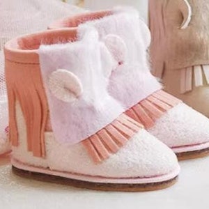 Op de afbeelding: Een paar roze en witte peuterlaarsjes met franjes en een pluche witte rand. De laarsjes hebben een bruine zool.