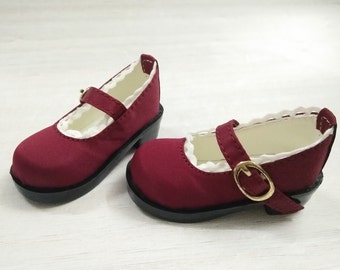 May include: A pair of burgundy doll shoes with a white lace trim and a gold buckle. The shoes have a black heel.
