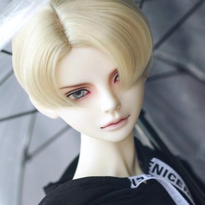 May include: A doll with a blonde wig styled in a short, side-swept look. The doll is wearing a black hoodie with a white stripe and the word "NICE" printed on it.