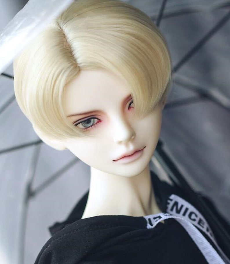 May include: A doll with a blonde wig styled in a short, side-swept look. The doll is wearing a black hoodie with a white stripe and the word "NICE" printed on it.