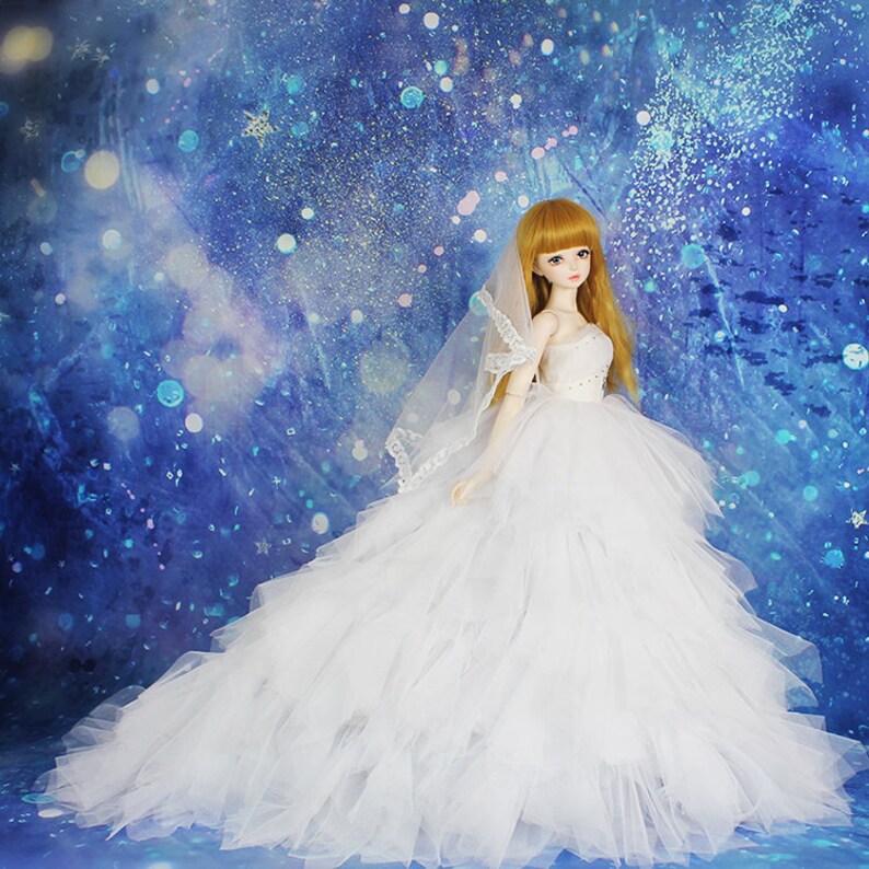 May include: A white bridal gown with a tulle skirt and a lace bodice. The doll is wearing a white veil and has long blonde hair.