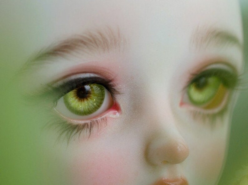 May include: Close-up of a doll's face with green eyes and long eyelashes. The doll has a light skin tone and a delicate, feminine appearance.