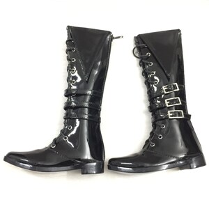 May include: A pair of black patent leather boots with lace-up fronts and buckle straps. The boots have a pointed toe and a low heel.