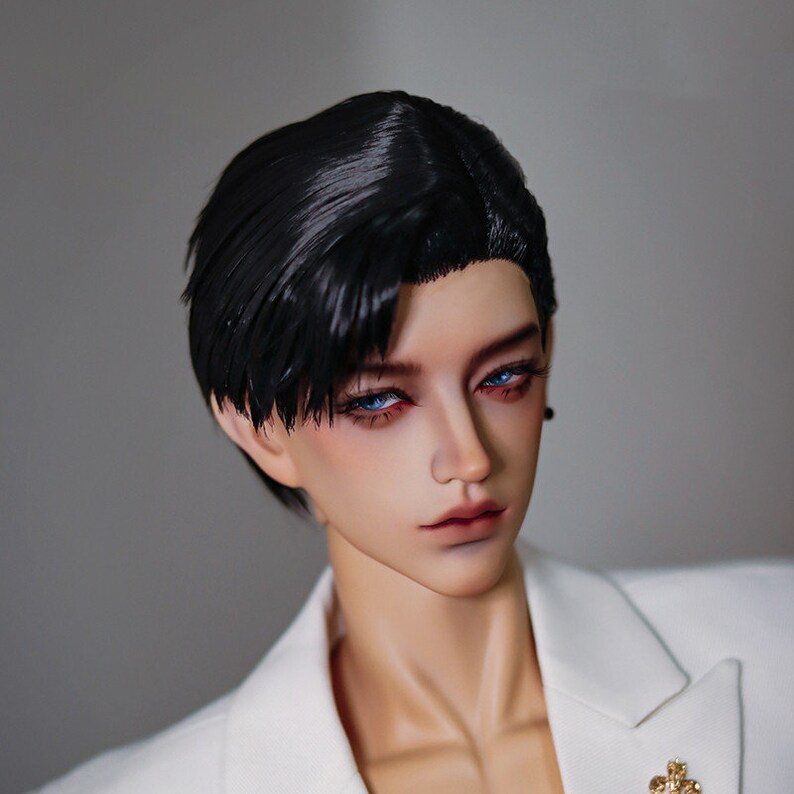 May include: A doll with short black hair styled in a side part, wearing a white blazer with a gold pin. The doll has blue eyes and a neutral expression.