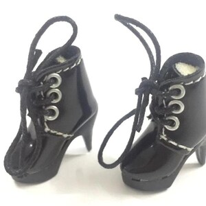 May include: A pair of black heeled boots with white stitching and silver eyelets. The boots have laces that tie at the ankle.