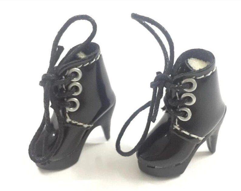 May include: A pair of black heeled boots with white stitching and silver eyelets. The boots have laces that tie at the ankle.