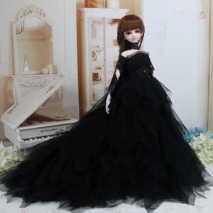 May include: A black tulle ball gown with a lace bodice and a black choker. The doll is wearing the gown and has long brown hair and blue eyes.