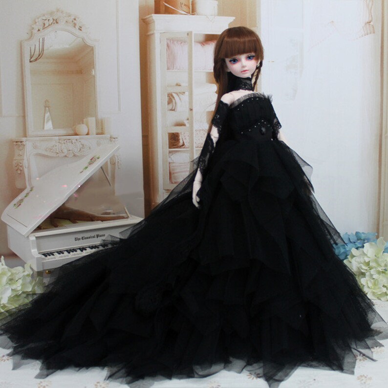 May include: A black tulle ball gown with a lace bodice and a black choker. The doll is wearing the gown and has long brown hair and blue eyes.