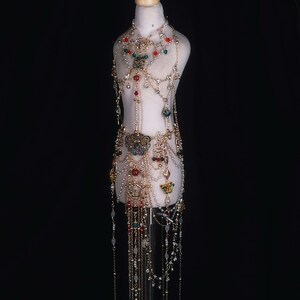 May include: A gold-toned body chain with red, green, and clear beads. The chain has a butterfly design and is layered with multiple strands of beads and chains.