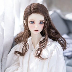 May include: A doll with long brown wavy hair, wearing a white blouse. The doll has blue eyes and a light skin tone.