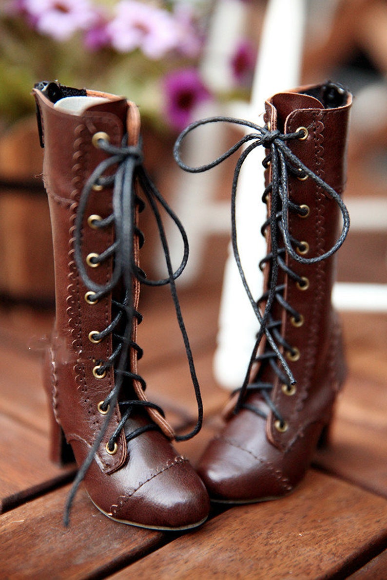 May include: A pair of brown leather boots with black laces and small heels. The boots have a vintage style with decorative stitching and brass eyelets. The laces are tied in bows, and the boots are set against a blurred background.