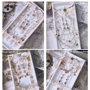 May include: Four sets of doll jewelry, each including a crown, necklace, and earrings. The sets feature gold-tone metal, clear crystals, and colored stones in purple, green, blue, and sapphire. Text labels include Full Set, Purple, Green, Blue, and Sapphire.