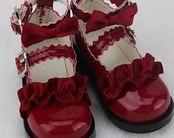 May include: A pair of red doll shoes with a black sole, white trim, and a red bow on each shoe.