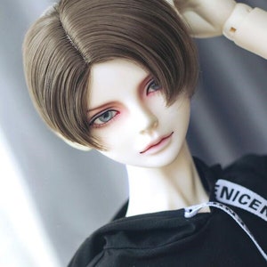 May include: A doll with brown hair styled in a short, side-swept cut. The doll is wearing a black hoodie with white text that reads "NICE".
