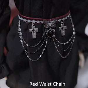 K&ouml;nnte beinhalten: Eine rote Taillenkette mit silbernen Kreuz- und Schmetterlingsanh&auml;ngern. Die Kette besteht aus mehreren Str&auml;ngen kleiner silberner Glieder.