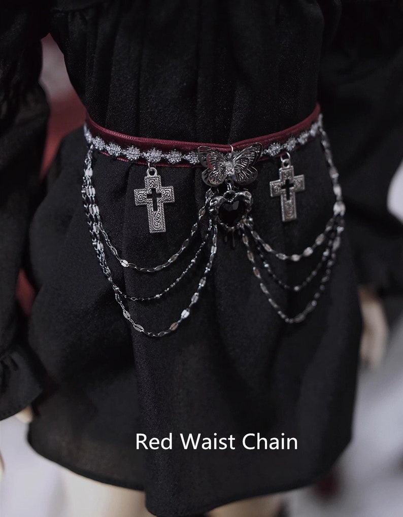 K&ouml;nnte beinhalten: Eine rote Taillenkette mit silbernen Kreuz- und Schmetterlingsanh&auml;ngern. Die Kette besteht aus mehreren Str&auml;ngen kleiner silberner Glieder.