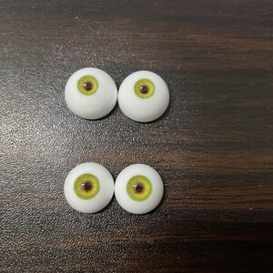 May include: Four doll eyes with white irises and green and brown pupils.