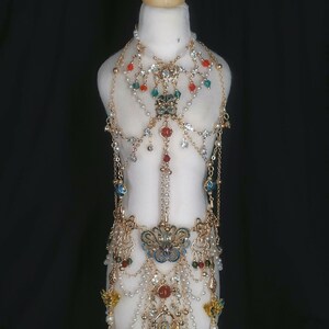 May include: A gold-tone body chain with multiple layers of beads and charms. The chain features a large, ornate pendant with blue and green enamel. The chain is decorated with red, green, and white beads.
