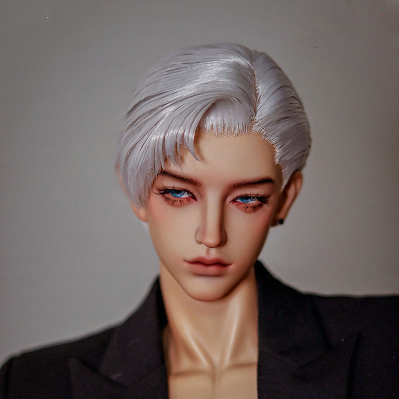 May include: A doll with short, silver-white hair styled in a side part. The doll has blue eyes and is wearing a black blazer.