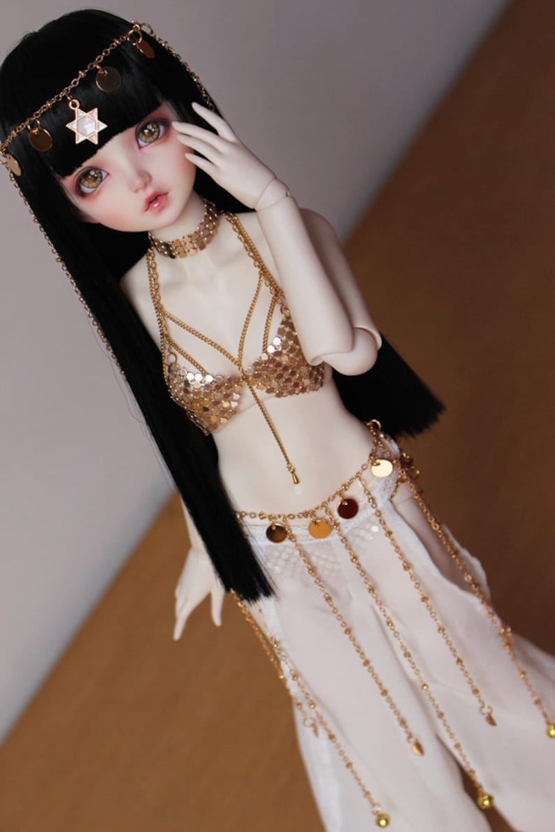 May include: A doll with long black hair wearing a gold sequined top and a white skirt with gold chains and coin accents.