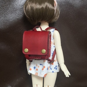 Puede incluir: Una mochila de cuero roja con hebillas de latón y un vestido de estampado floral blanco y naranja.