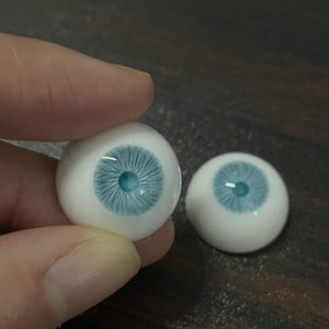 K&ouml;nnte beinhalten: Zwei blaue und wei&szlig;e Puppenaugen mit realistischer Iris und Pupille.