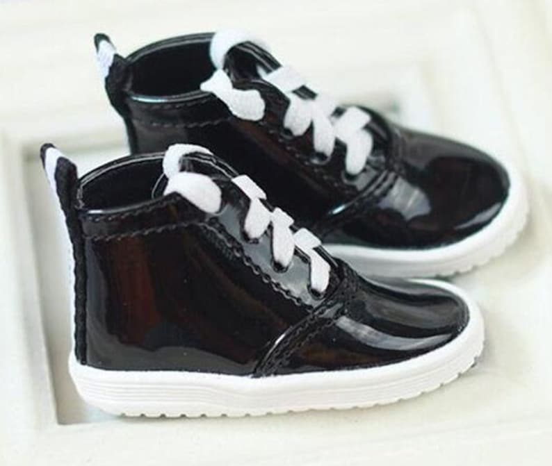 May include: A pair of black patent leather high-top sneakers with white laces and a white trim around the sole.